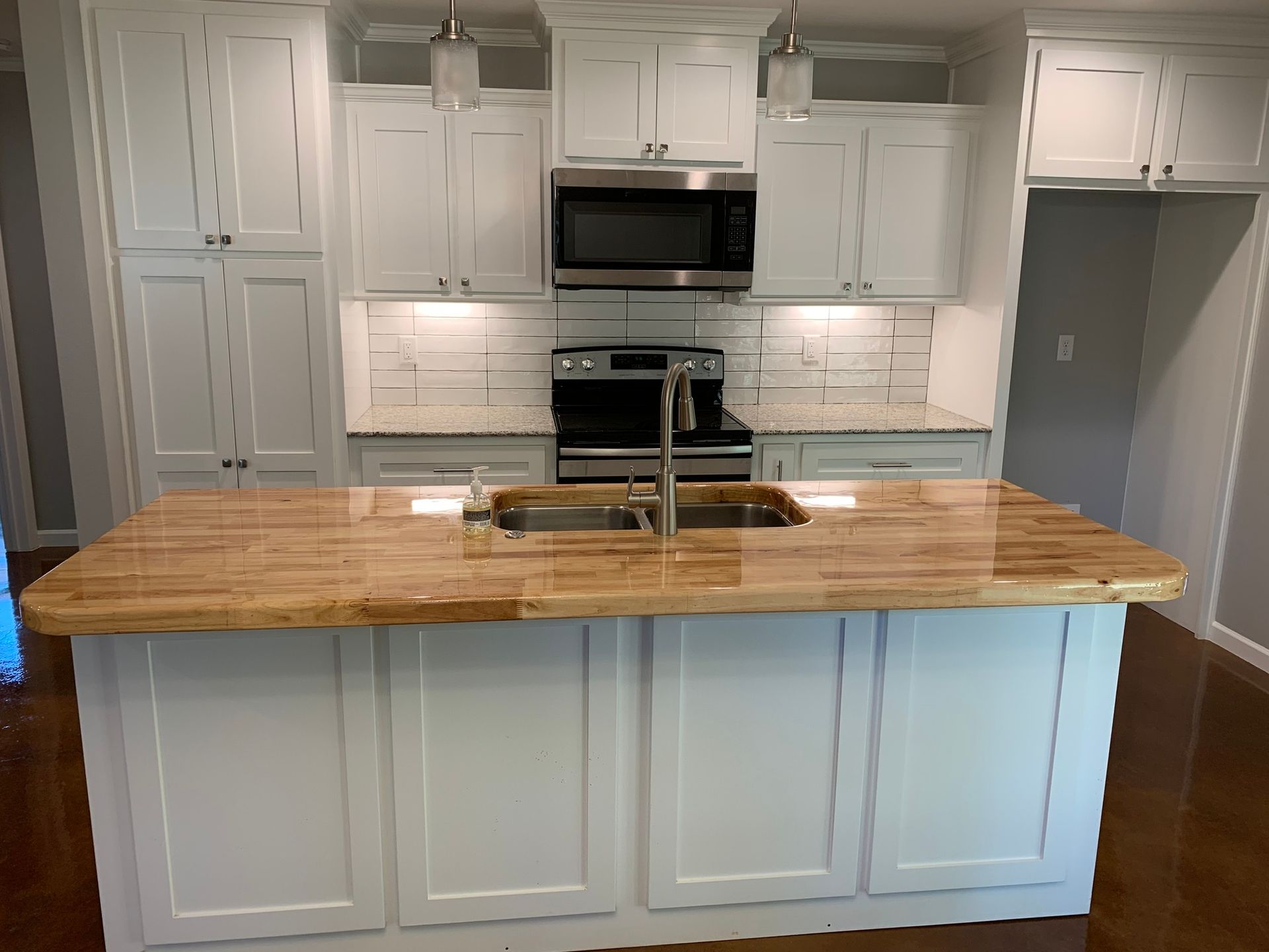 White kitchen with wood island countertop, stainless steel appliances, and white cabinets.