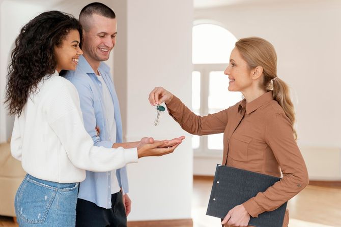 A woman is giving a man and woman keys to their new home.