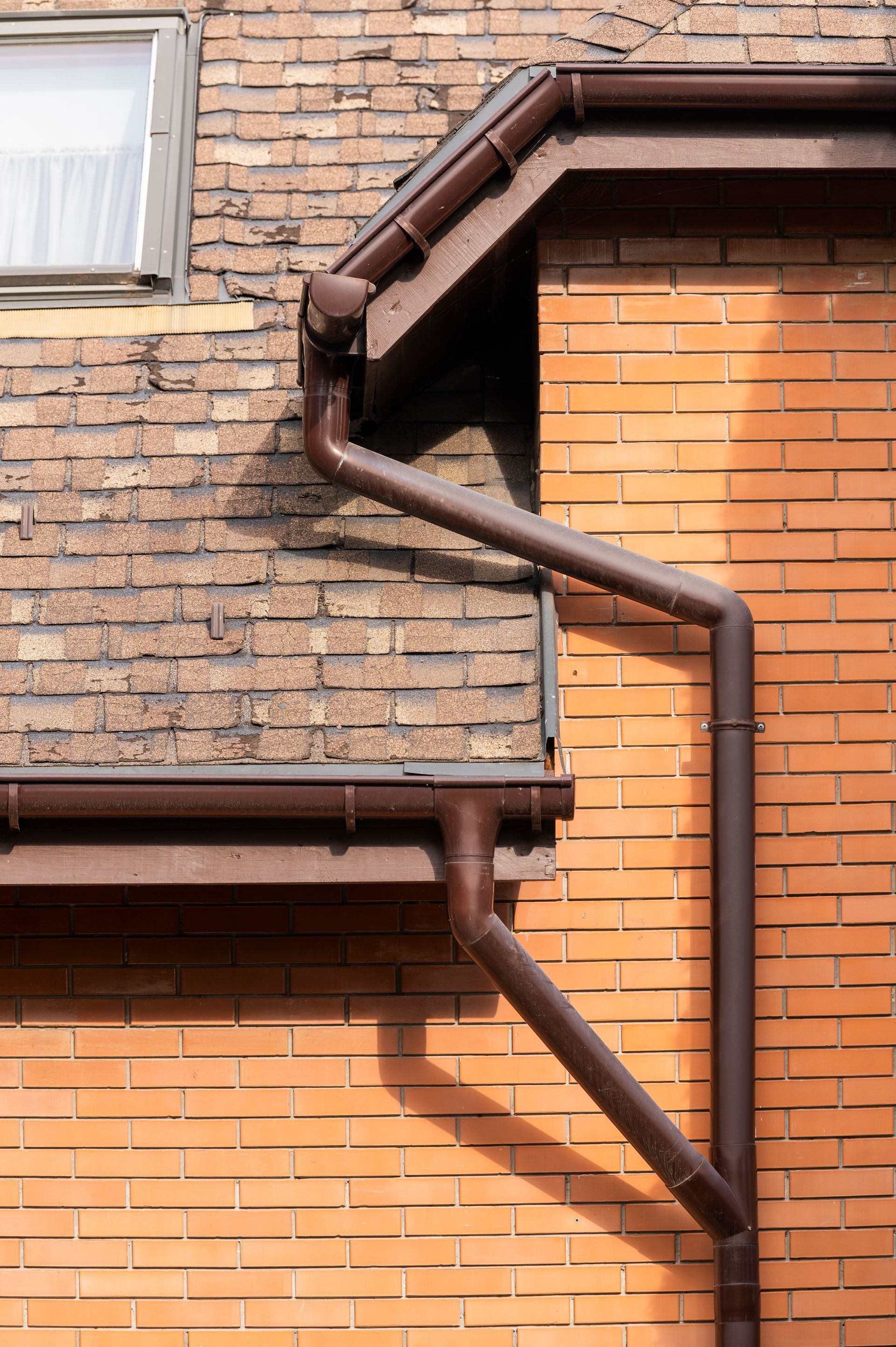 A brown gutter on the side of a brick building.