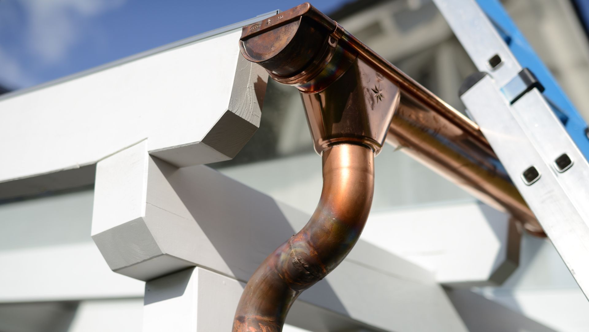 A close up of a copper gutter on a house with a ladder in the background.