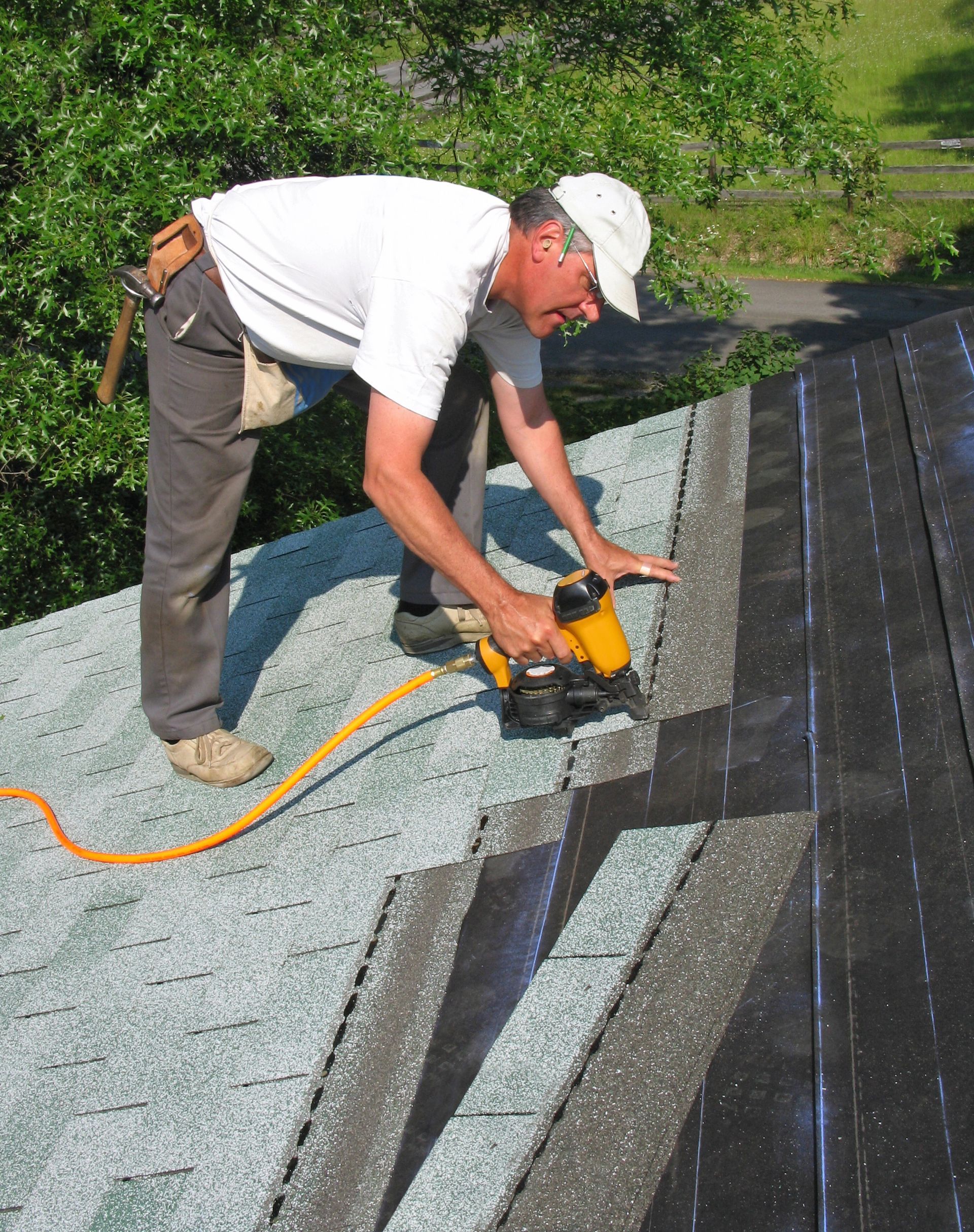 carpenter uses nail gun to attach asphalt shingles to roof