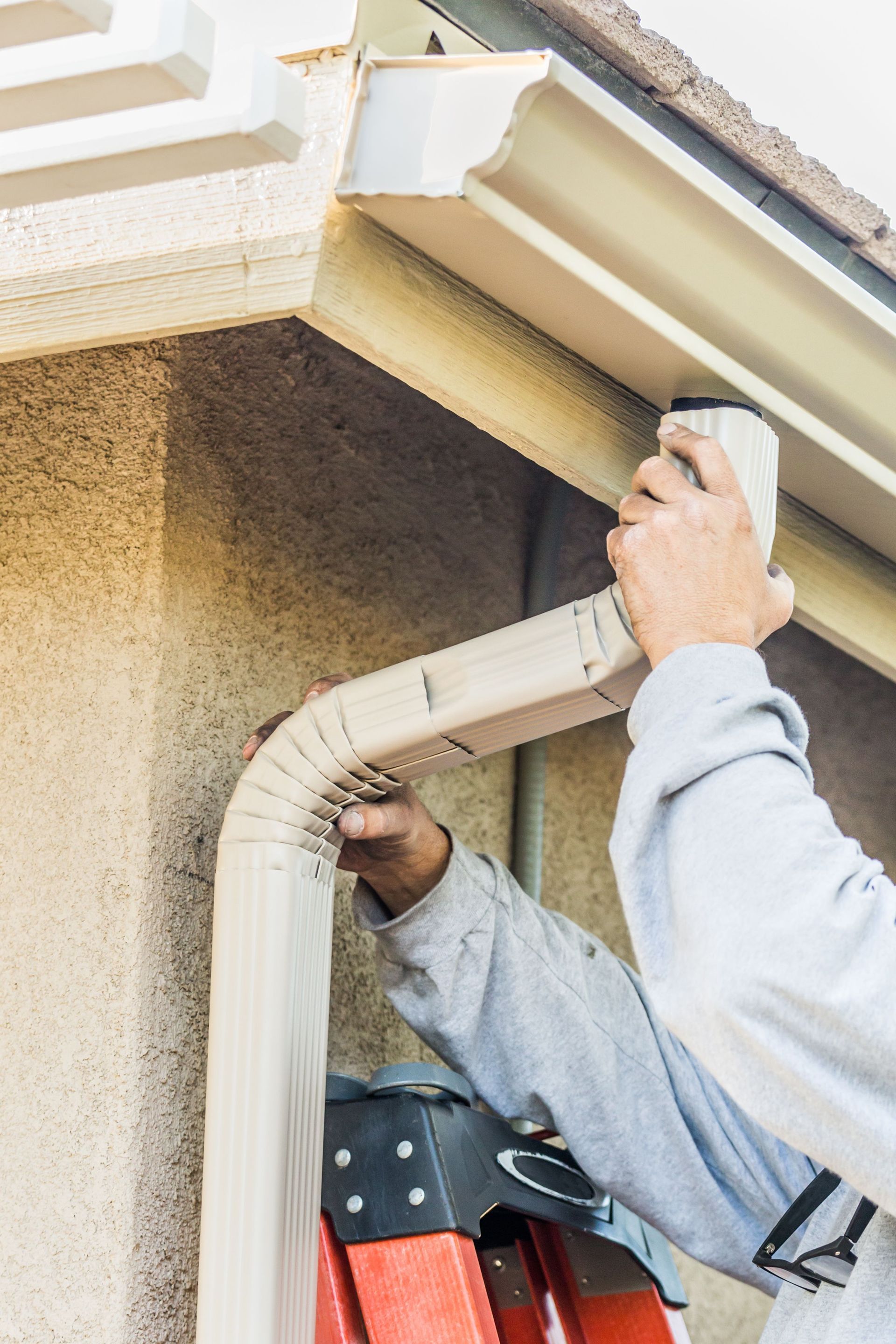 A man is standing on a ladder fixing a gutter on a house.