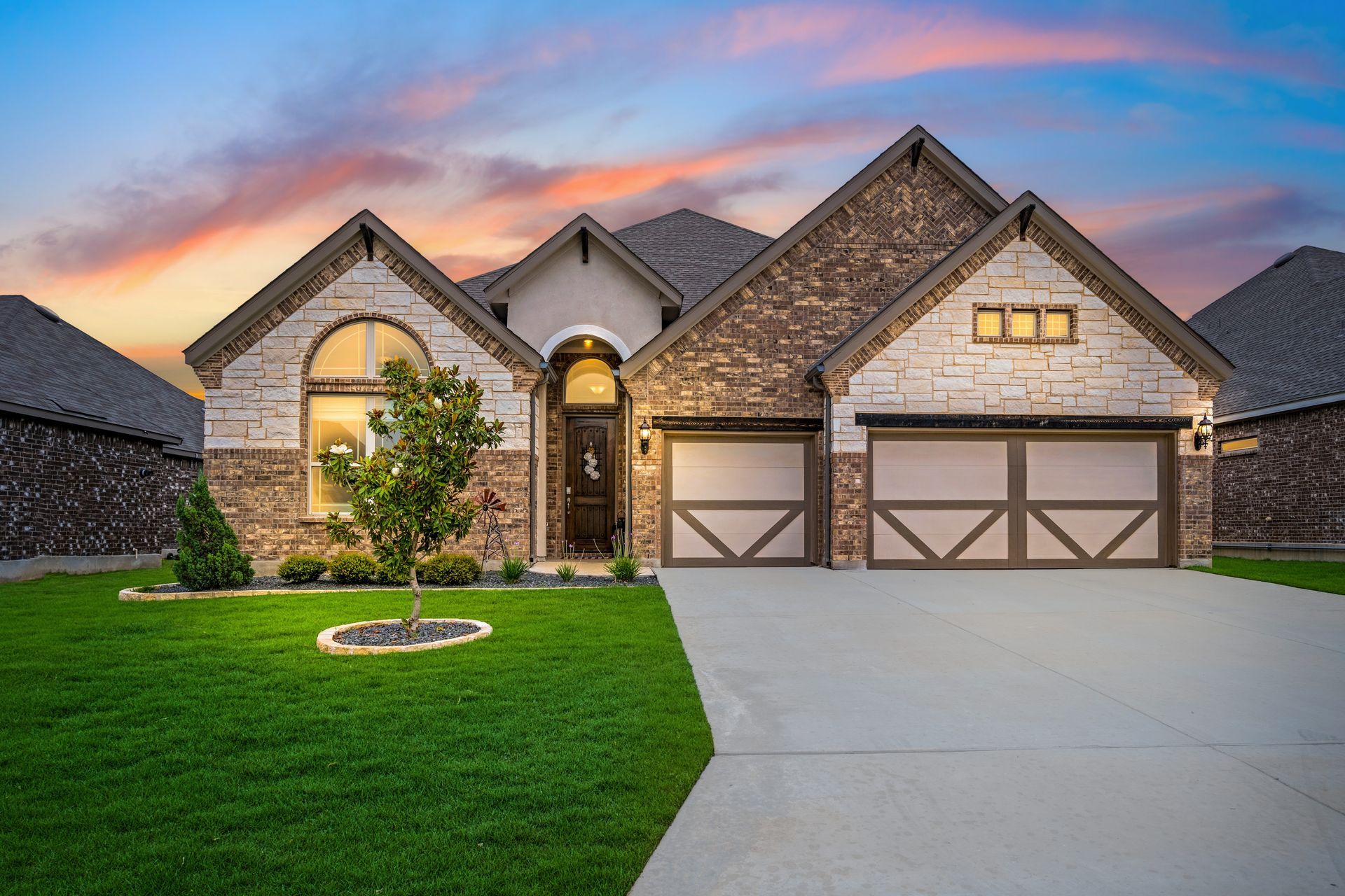 A large brick house with two garage doors and a lush green lawn.