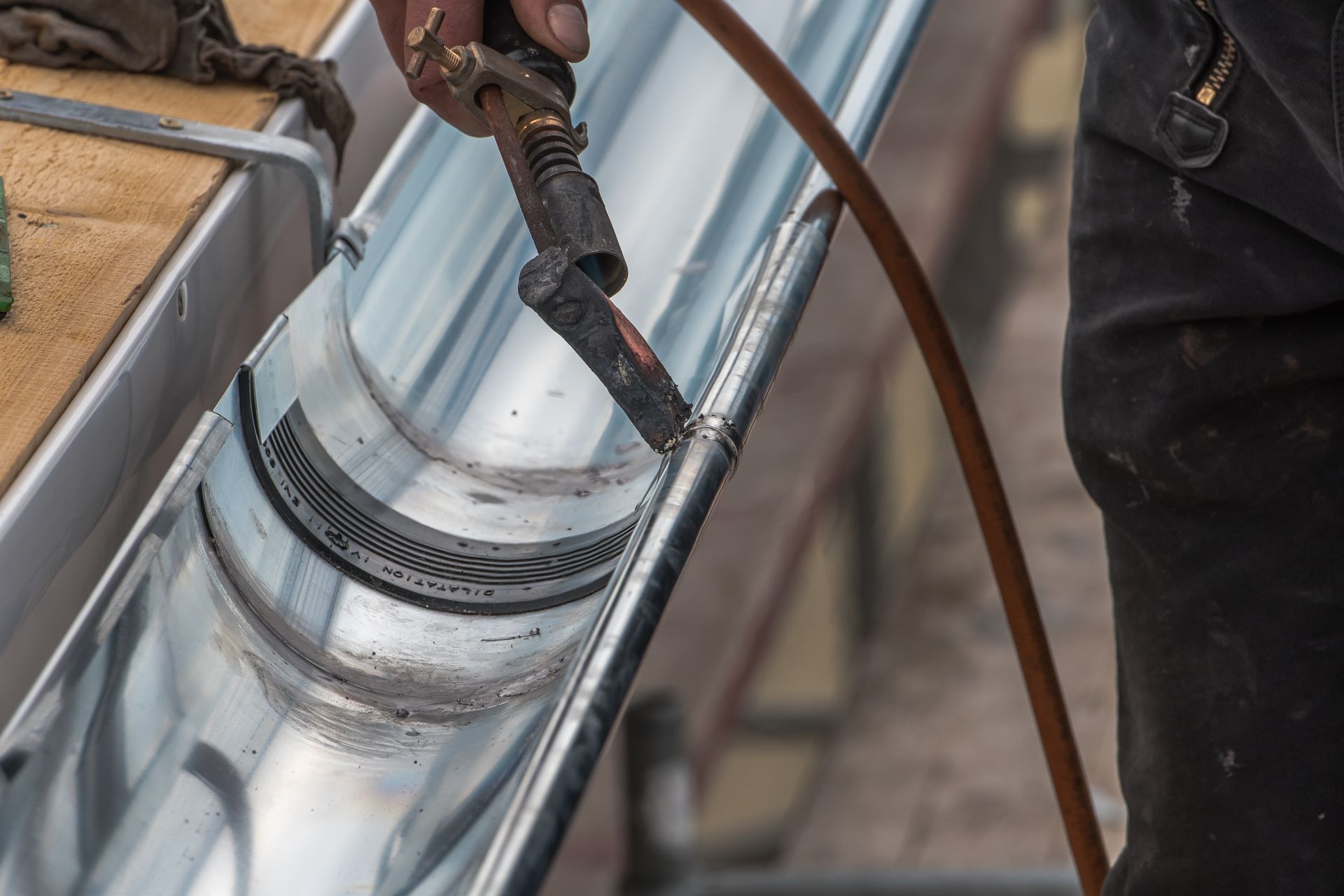 A man is welding a metal gutter with a torch.