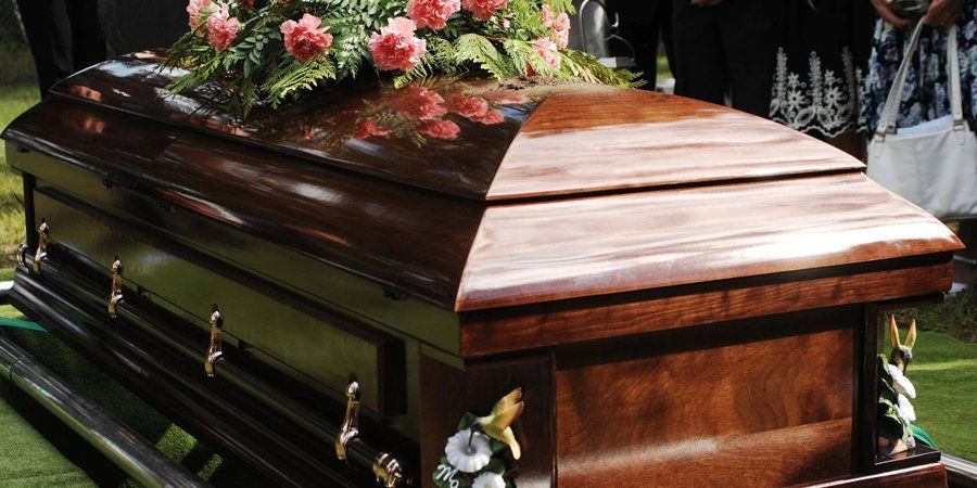 Wood casket at cemetery with casket flowers