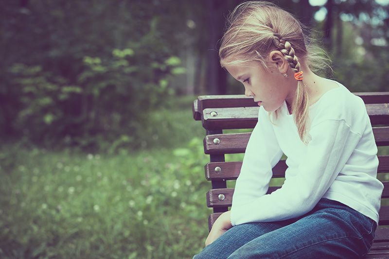 Sad little girl sitting on park bench by themselves