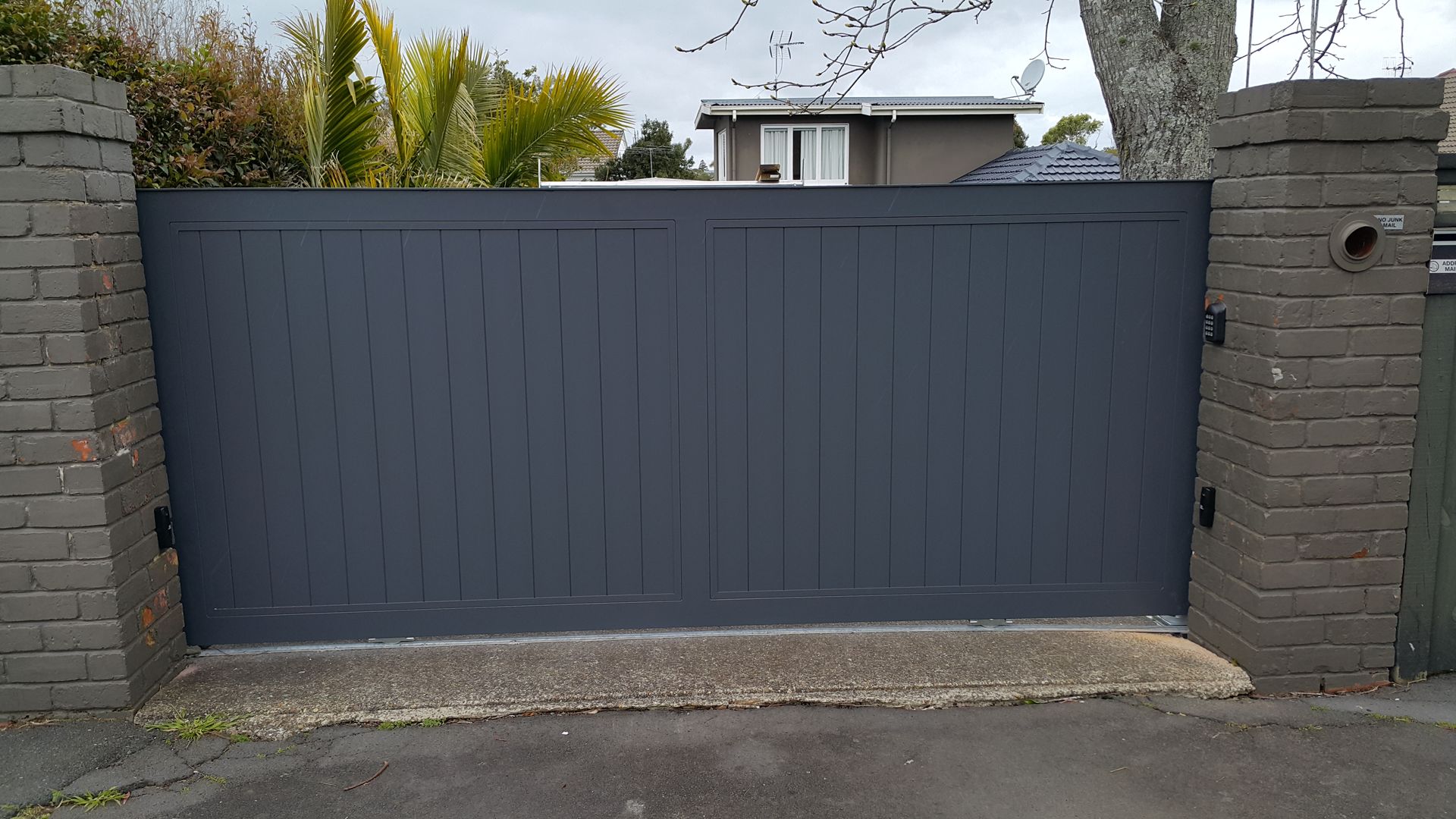 A gray gate is sitting in front of a brick wall.