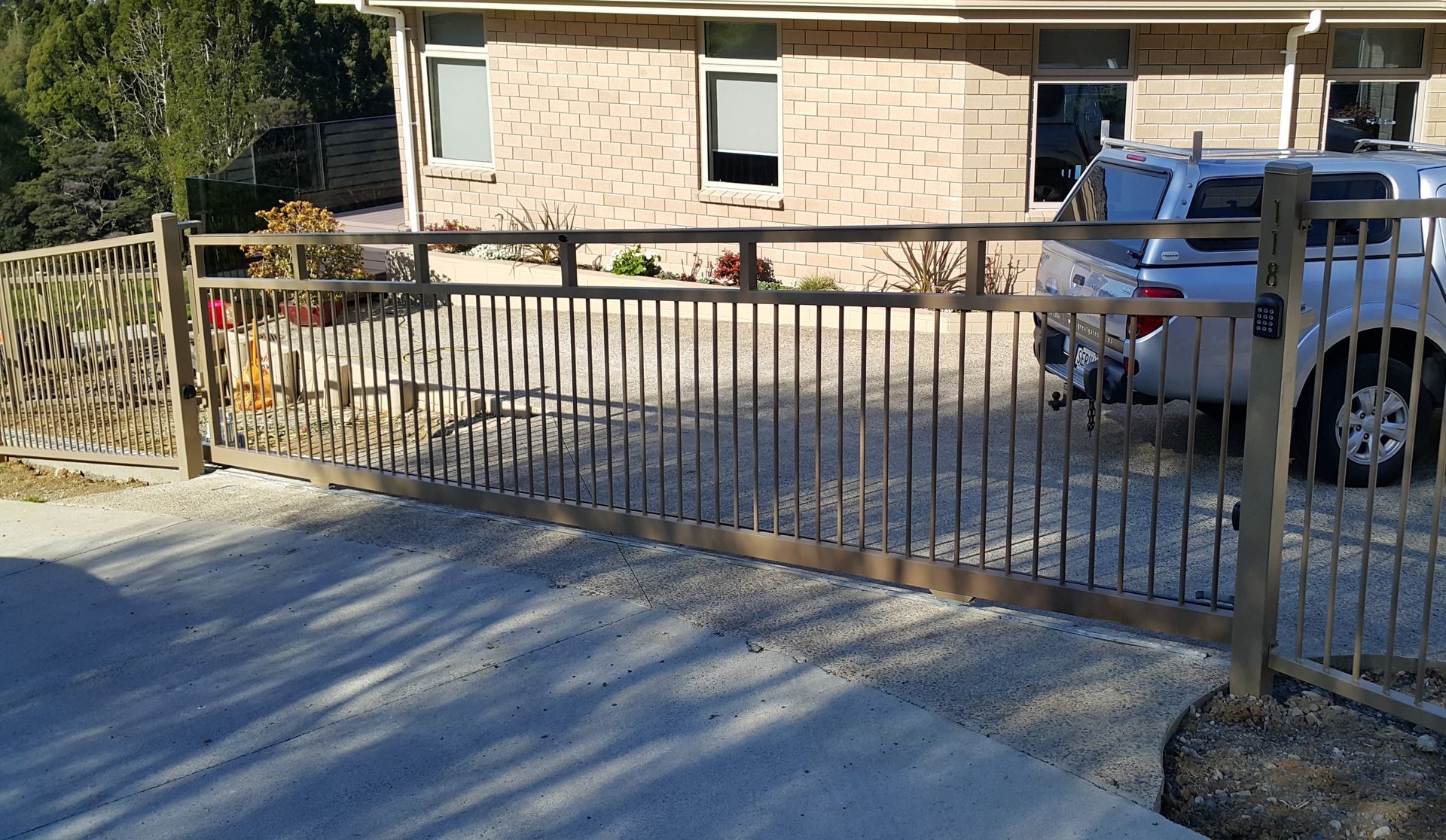A car is parked in front of a brick house behind a metal gate.
