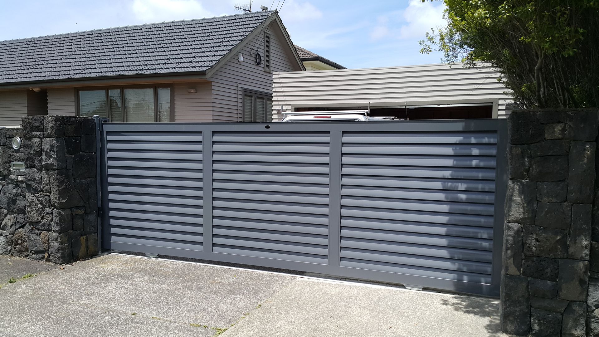 A sliding gate is open to a driveway in front of a house.