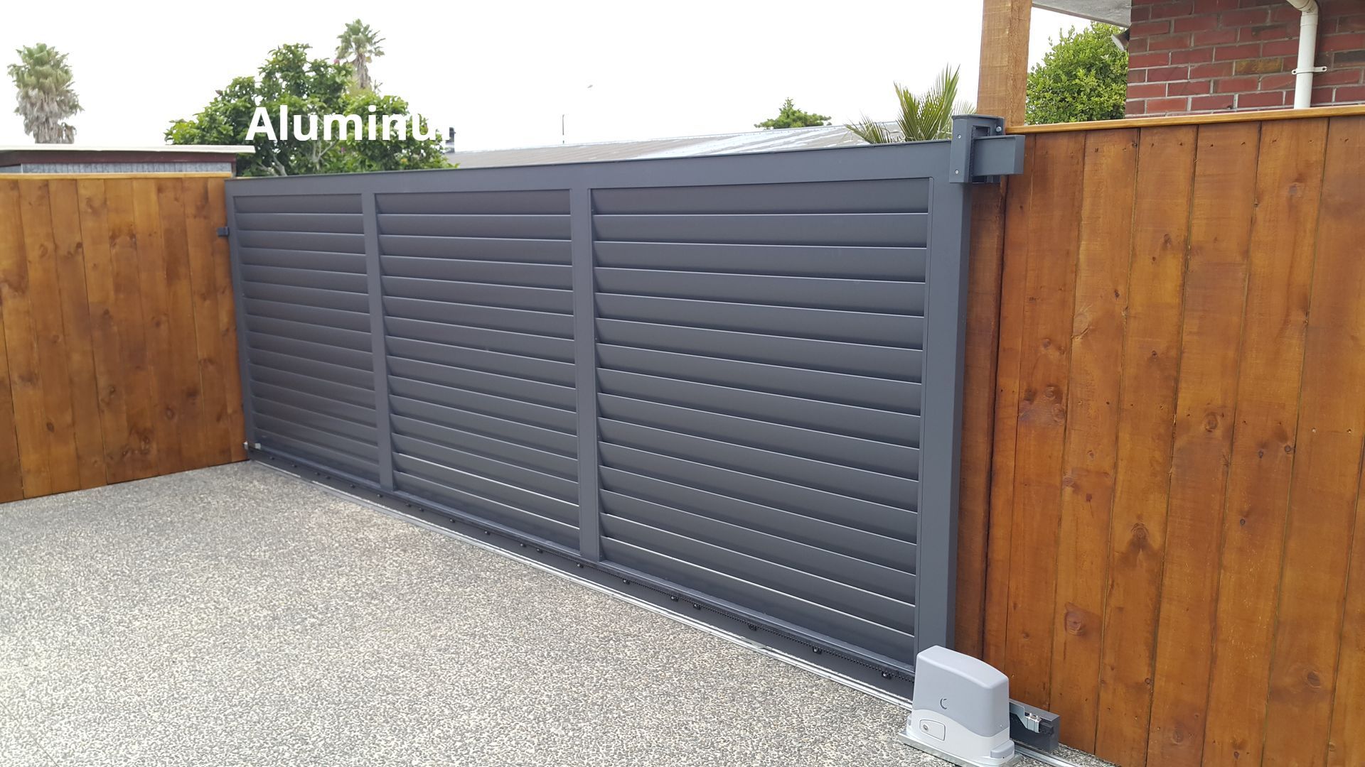 A gray sliding gate with a wooden fence behind it