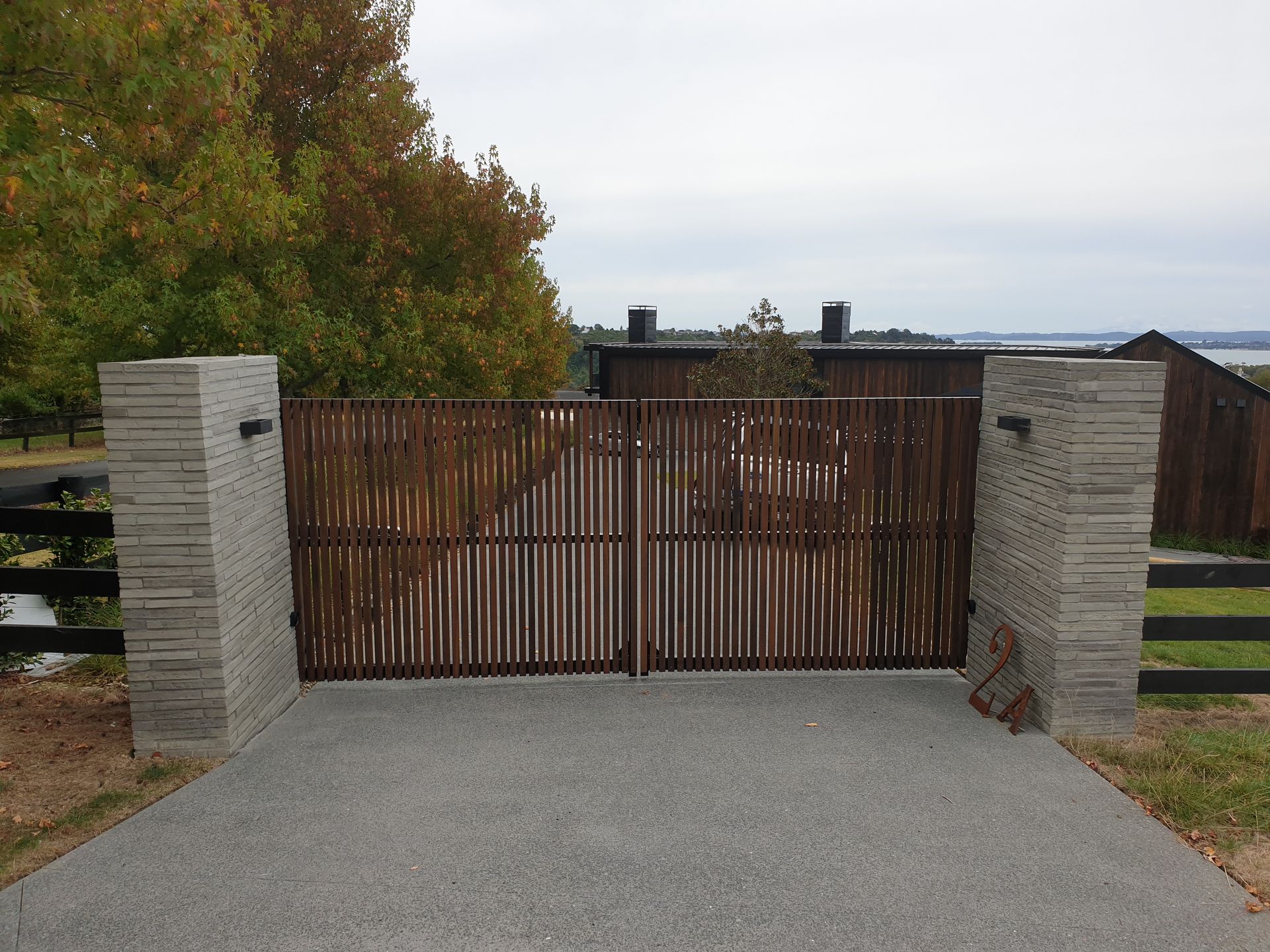 A concrete driveway with a wooden gate between two stone pillars