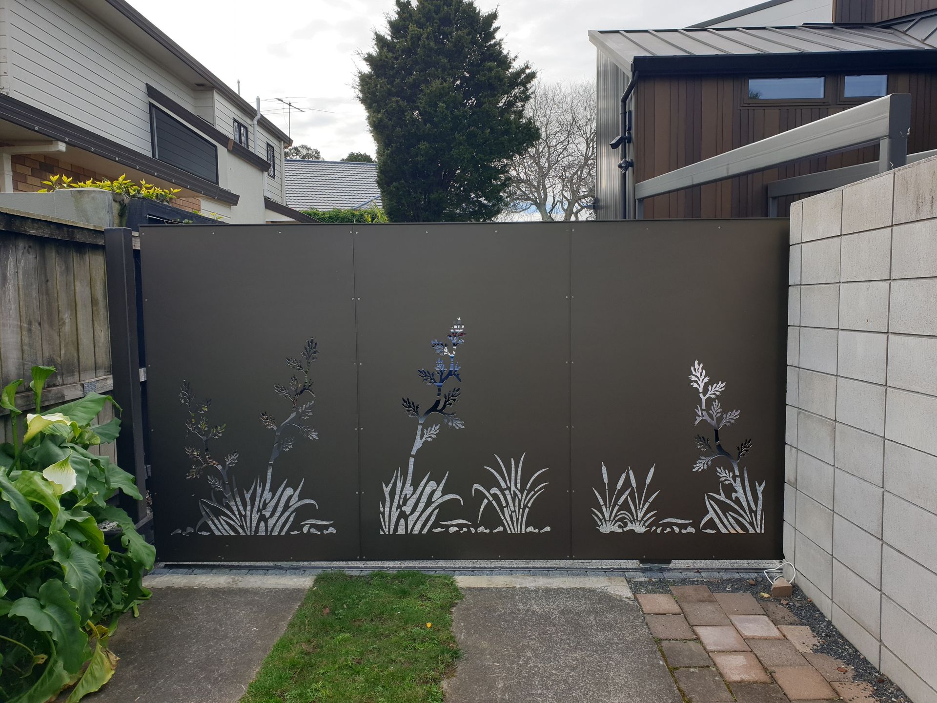 A sliding gate with a floral design on it is in front of a house.