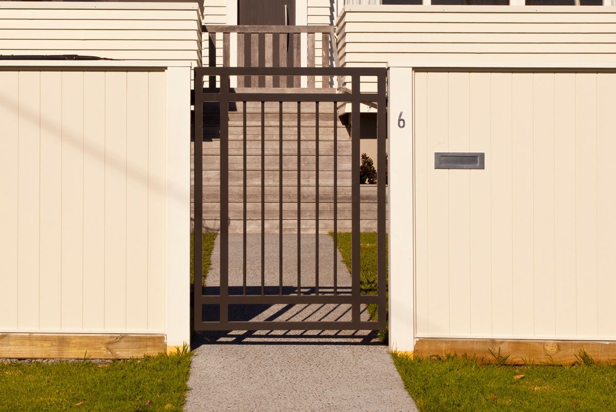 A white fence with a black gate leading to a house.