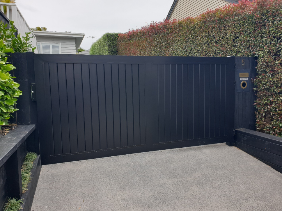 A black sliding gate is sitting in the middle of a driveway.