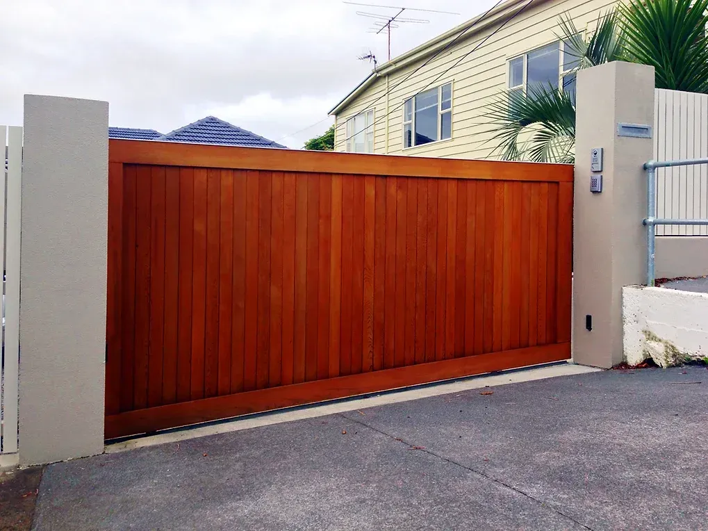 A wooden gate is open to a driveway in front of a house
