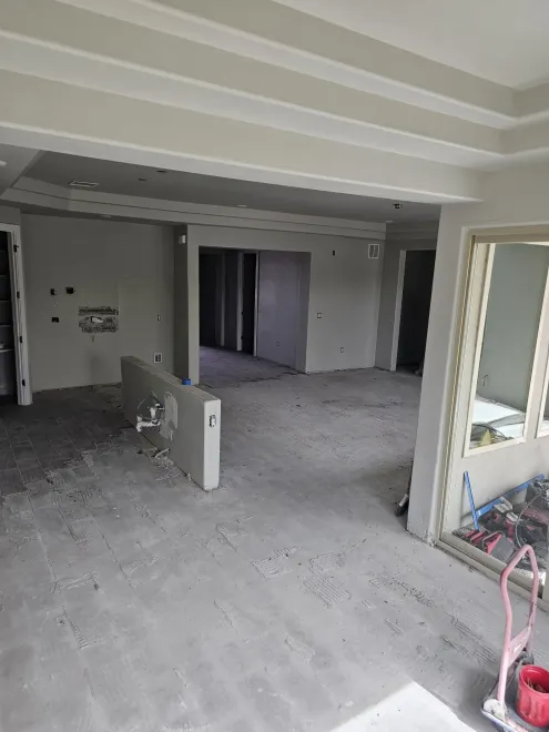 An interior view of a room under construction, showing grey unfinished floors, walls, and a partial partition wall.