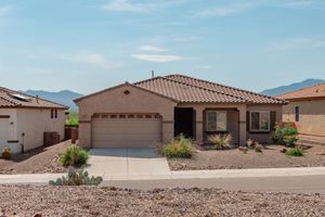 A single-story, tan stucco suburban house with a tile roof, a two-car garage, and desert landscaping.