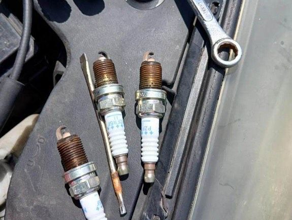 Three spark plugs are sitting on the hood of a car next to a wrench.