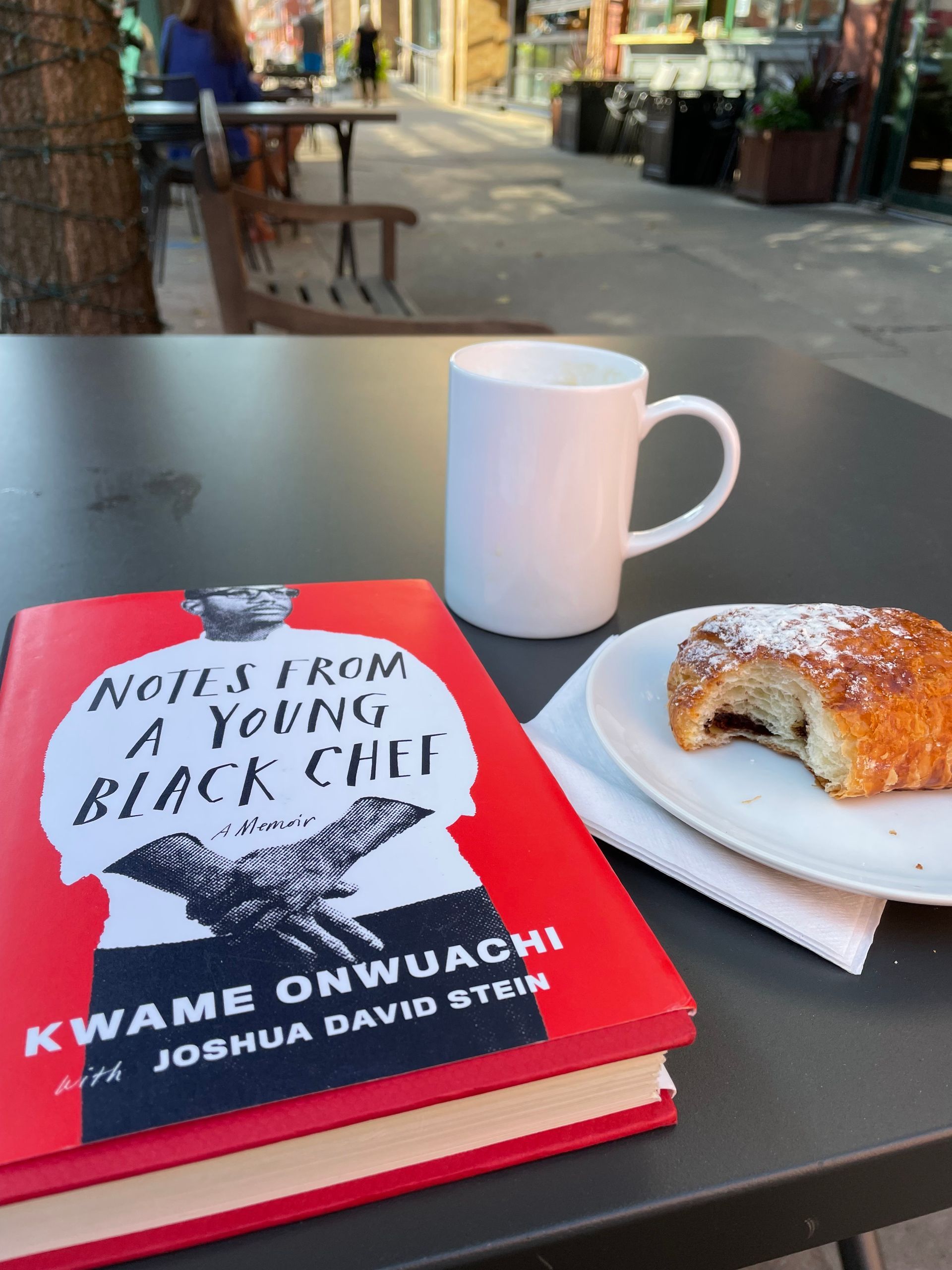 close up of a cup of coffee, pastry, and a book at a cafe