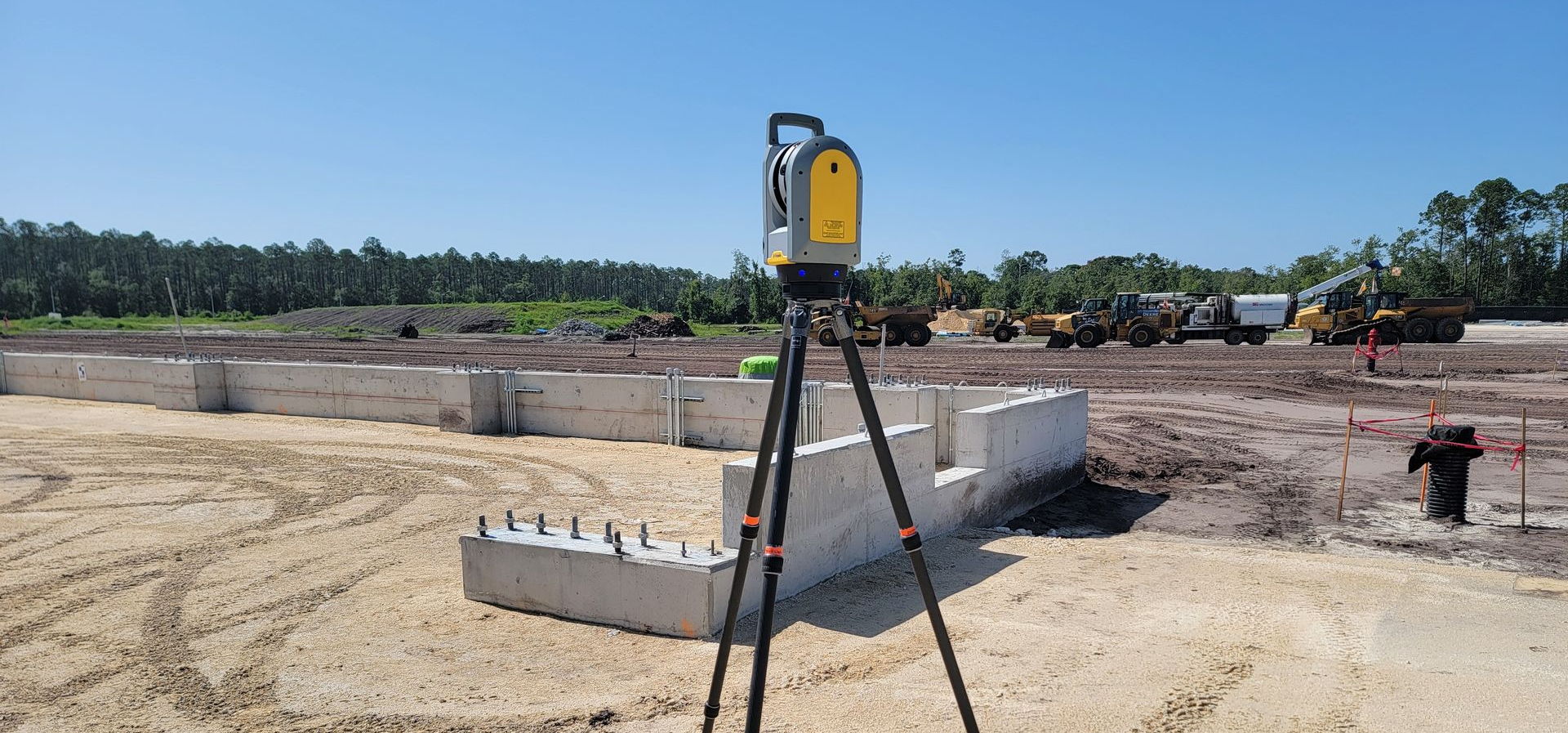 Terrestrial LiDAR scanning of as-built anchor bolts in a hangar's concrete foundation, with construction equipment in the background on a clear day.