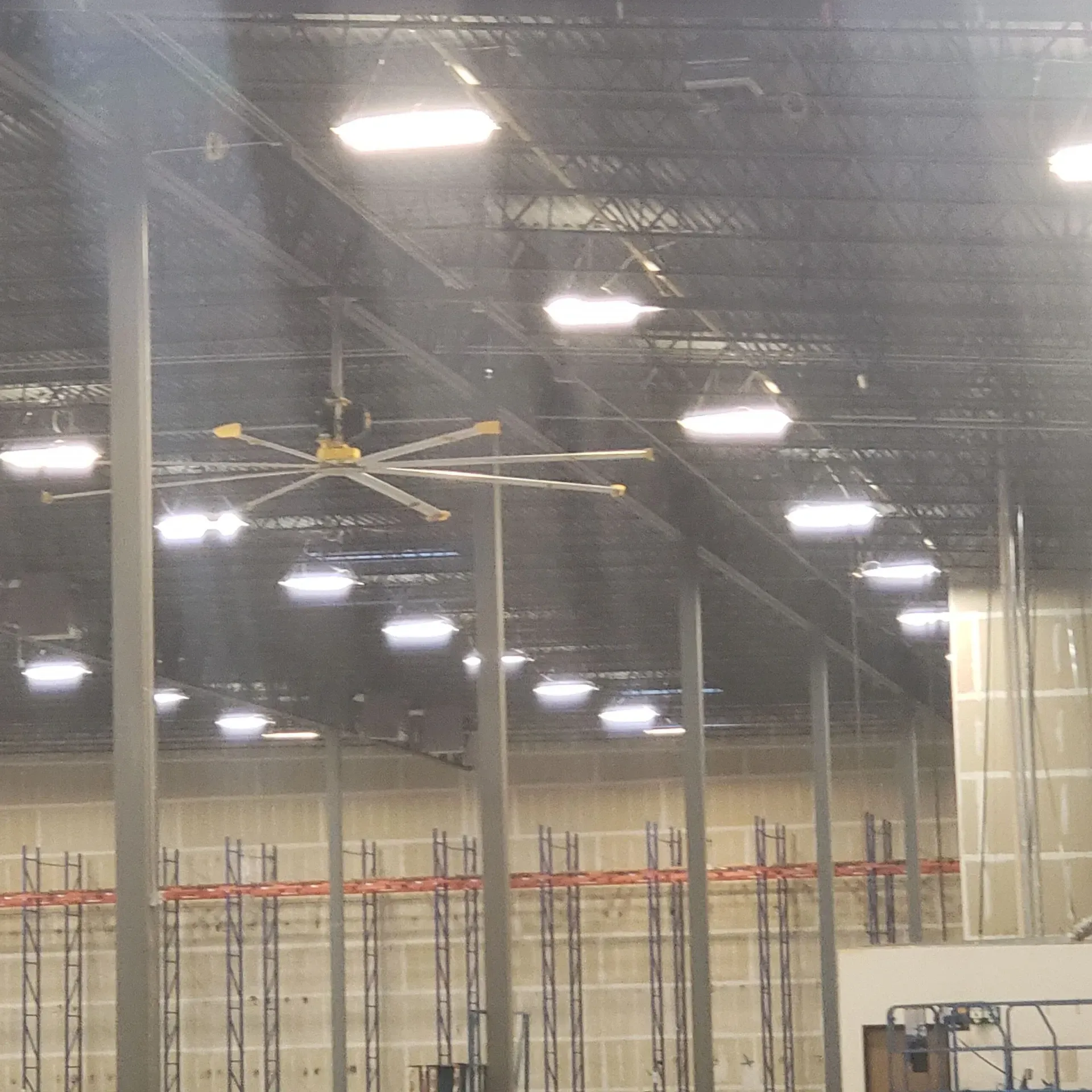A large ceiling fan is hanging from the ceiling of a warehouse