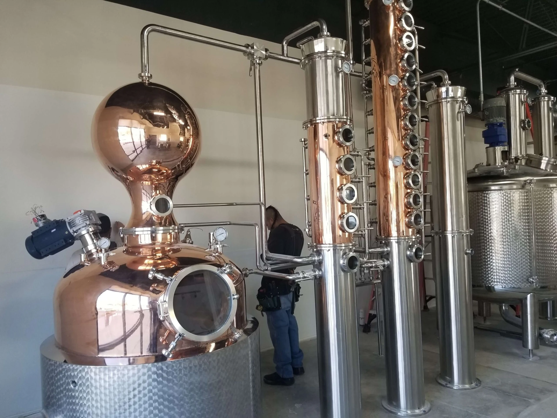 A woman is standing in front of a large copper distillery.
