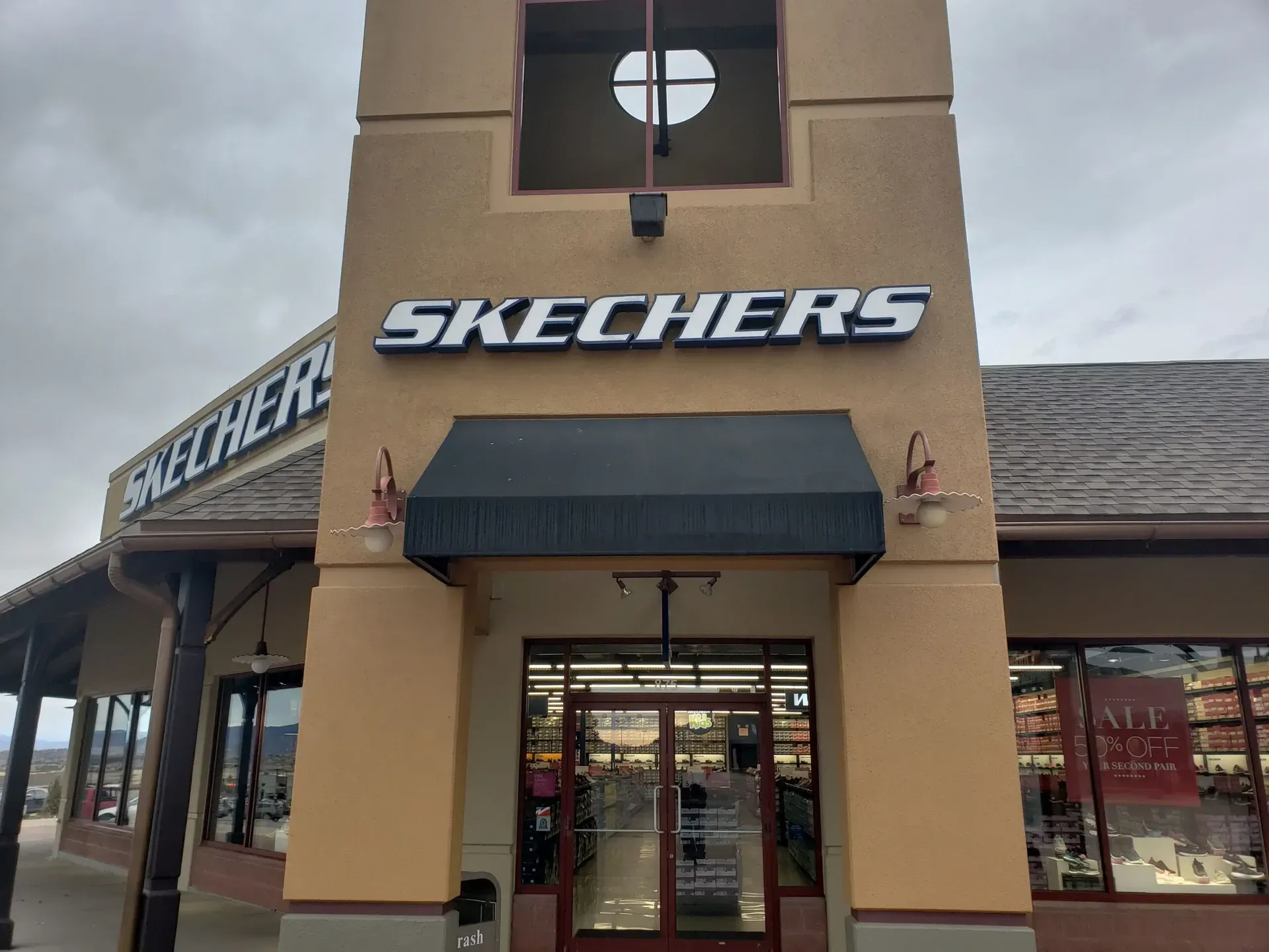 The front of a skechers store with a black awning
