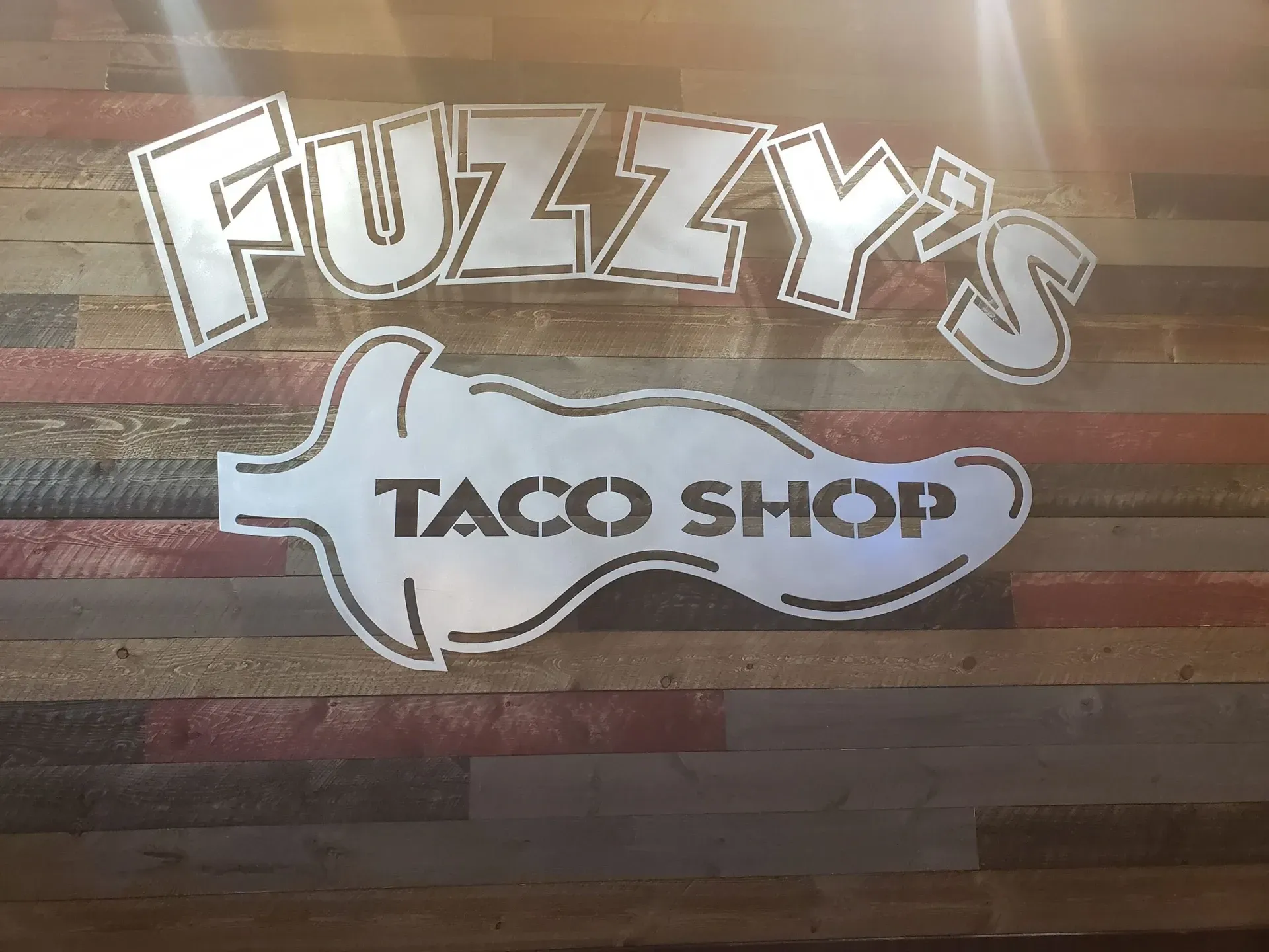 A fuzzy 's taco shop sign on a wooden wall