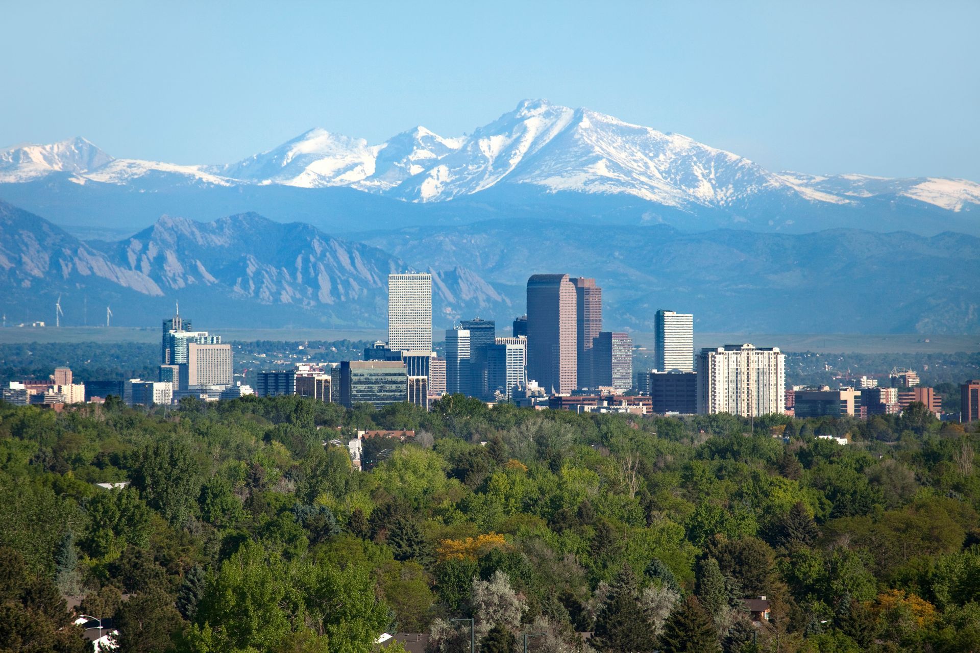 A city skyline with mountains in the background and trees in the foreground.