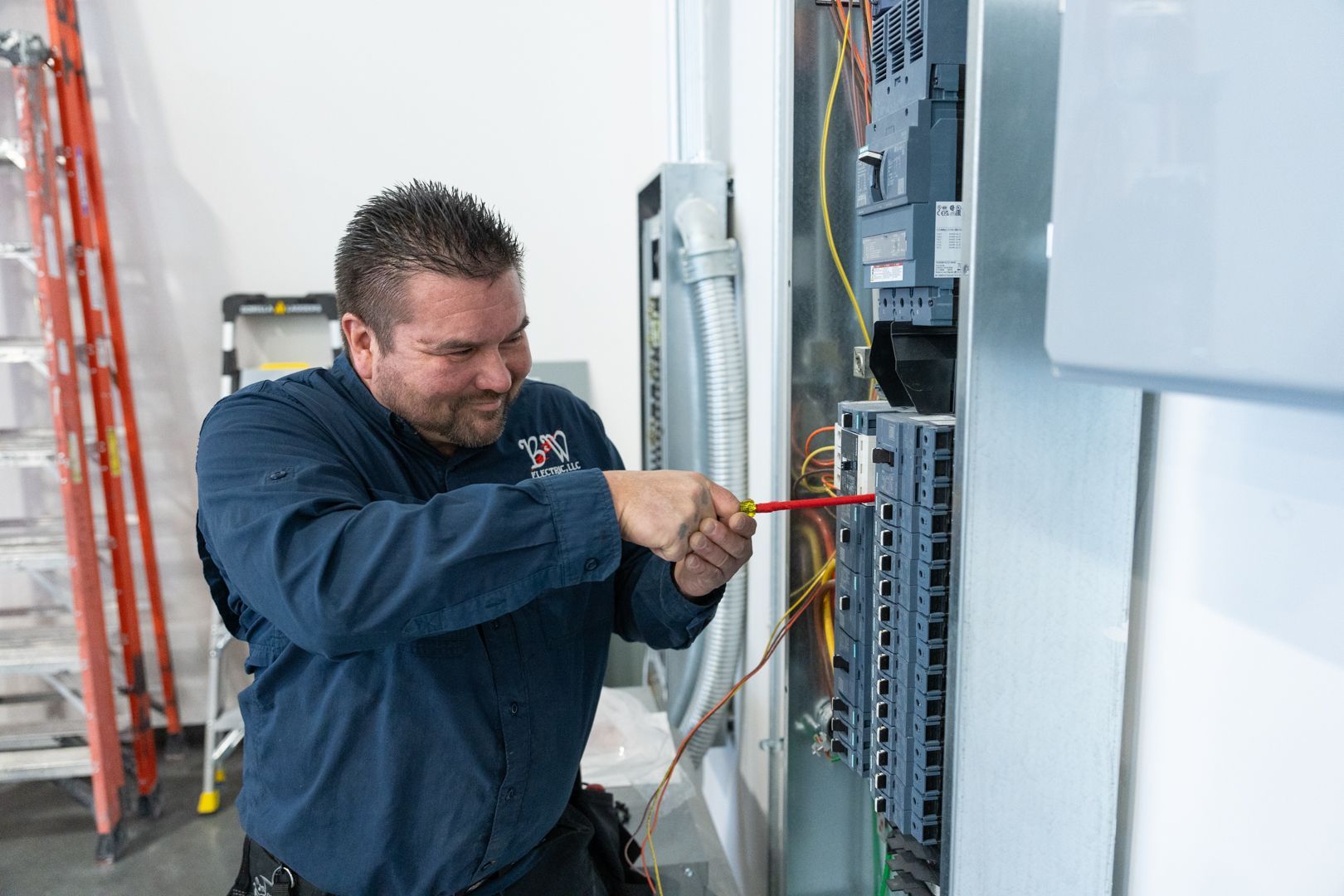 A B & W Services Technician is working on an electrical box with a screwdriver.
