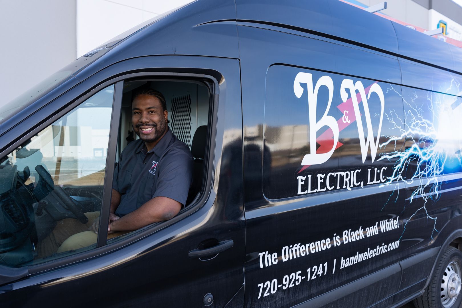 A B & W Services Technician is sitting in the driver 's seat of an electric van.