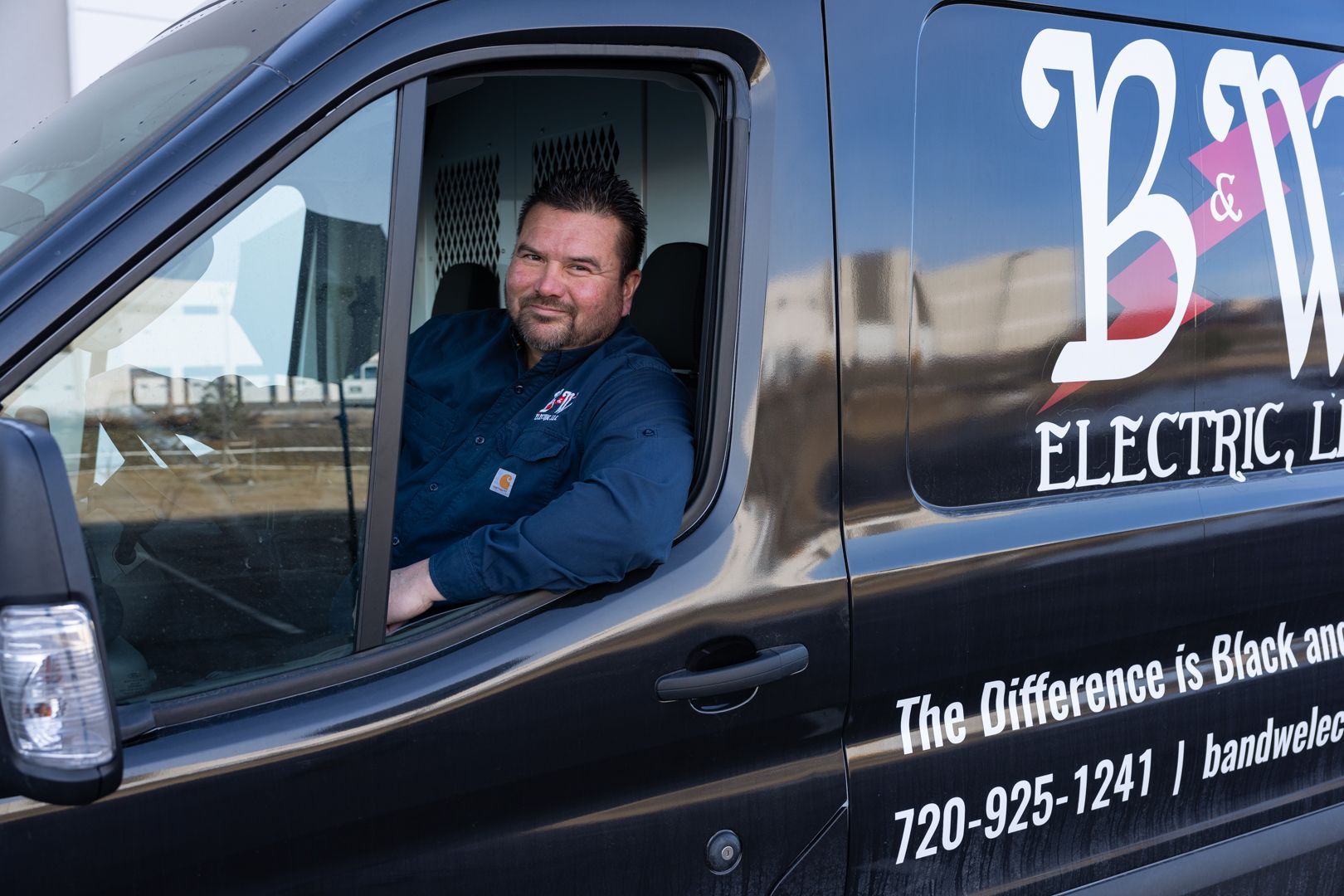 A B & W Services Technician is sitting in the driver 's seat of a black van.