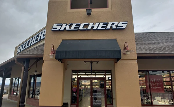 The front of a skechers store with a black awning