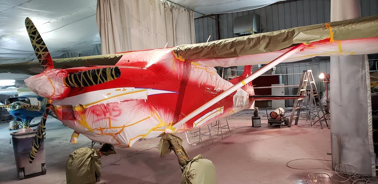 Airplane being painted red inside a hangar. Wings and tail masked off.