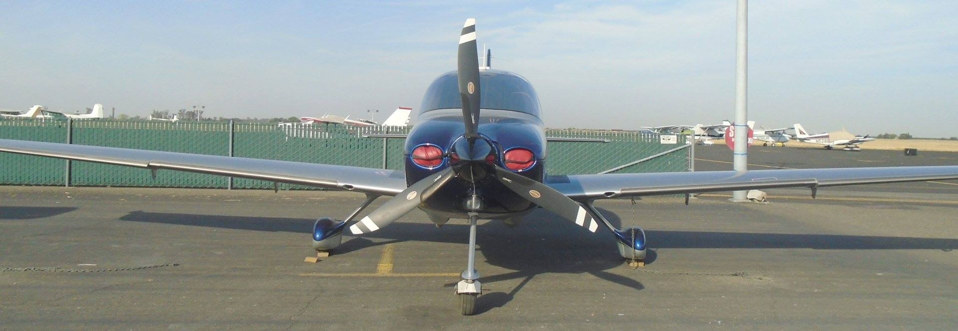 Blue airplane on tarmac, facing camera with propeller, wings extended.
