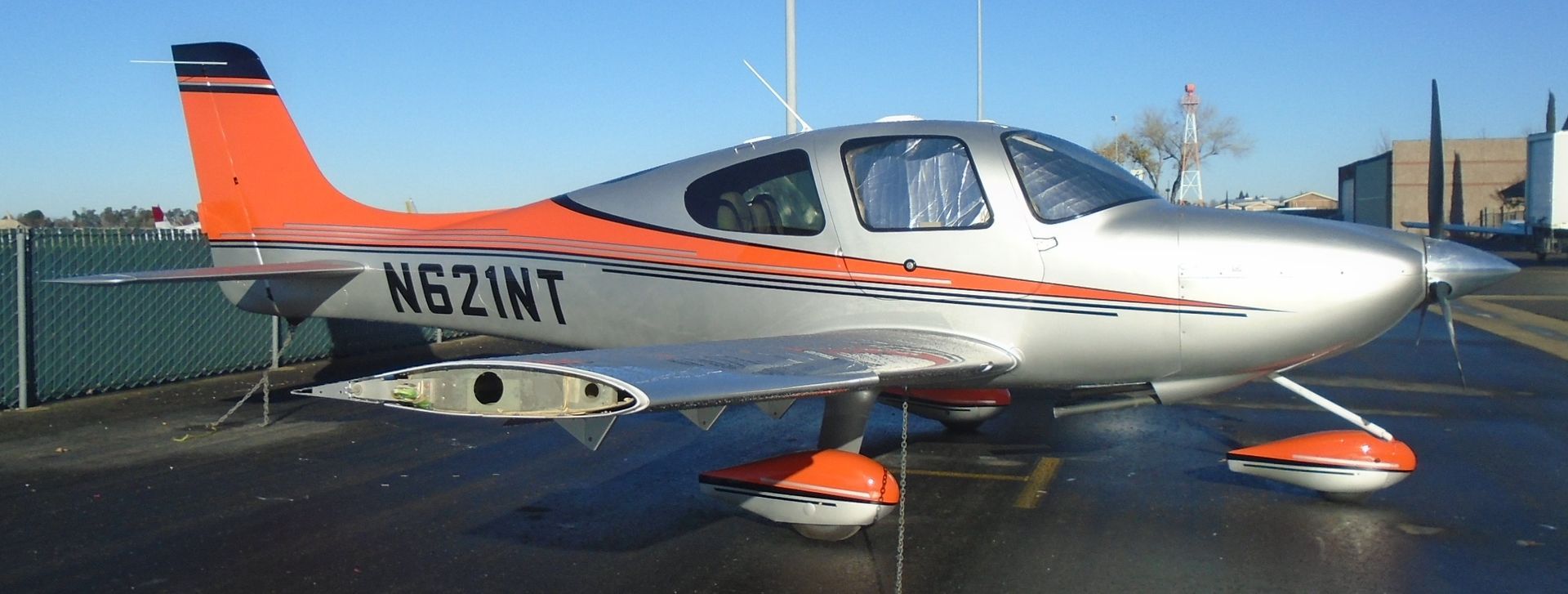 Silver and orange small airplane on the ground, registration N621MT.