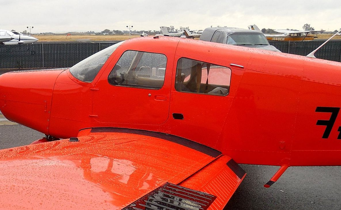 Red airplane on the ground at an airfield, with a partially visible wing and the cockpit windows.