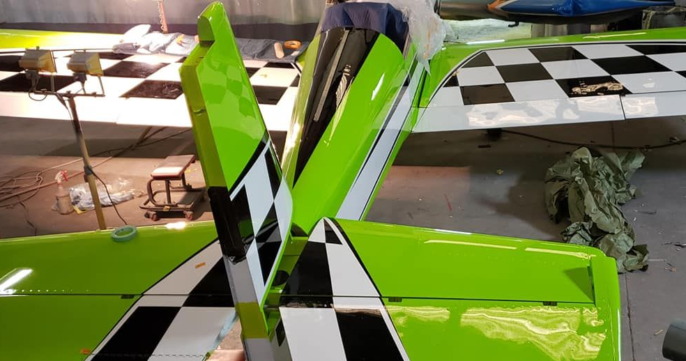 A bright green and black stunt plane's wings and tail, set in a workshop with checkered wings.