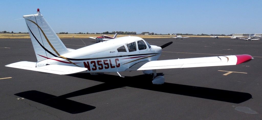 White and red airplane on a tarmac, with the registration N355LC. Blue sky in the background.