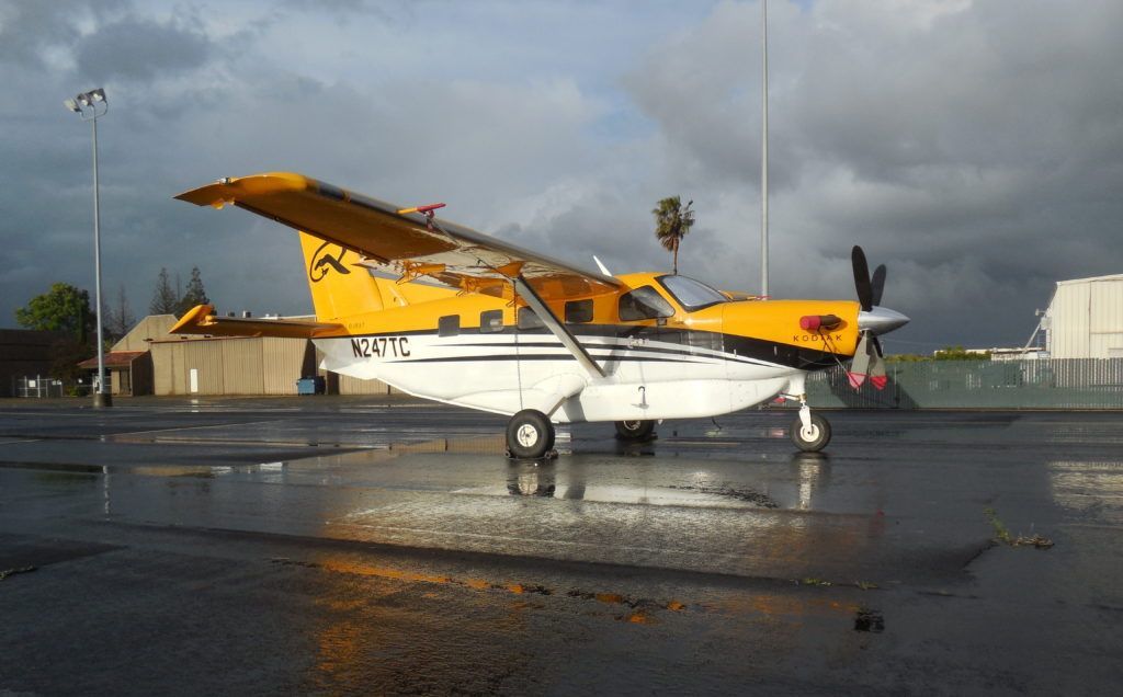 Yellow and white bush plane on a wet tarmac, with a dark, cloudy sky overhead.