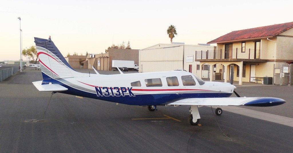 A small, blue and white airplane parked on a tarmac; buildings in the background.