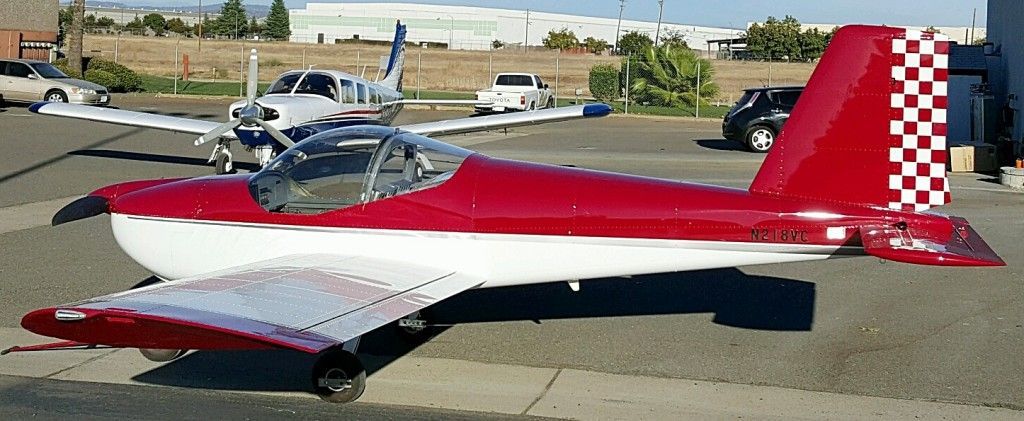 Red and white airplane with checkered tail parked on asphalt, another plane in the background.