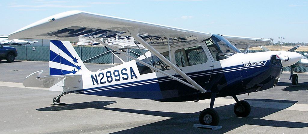 Blue and white single-engine airplane parked on a paved surface. The tail has a stylized design.