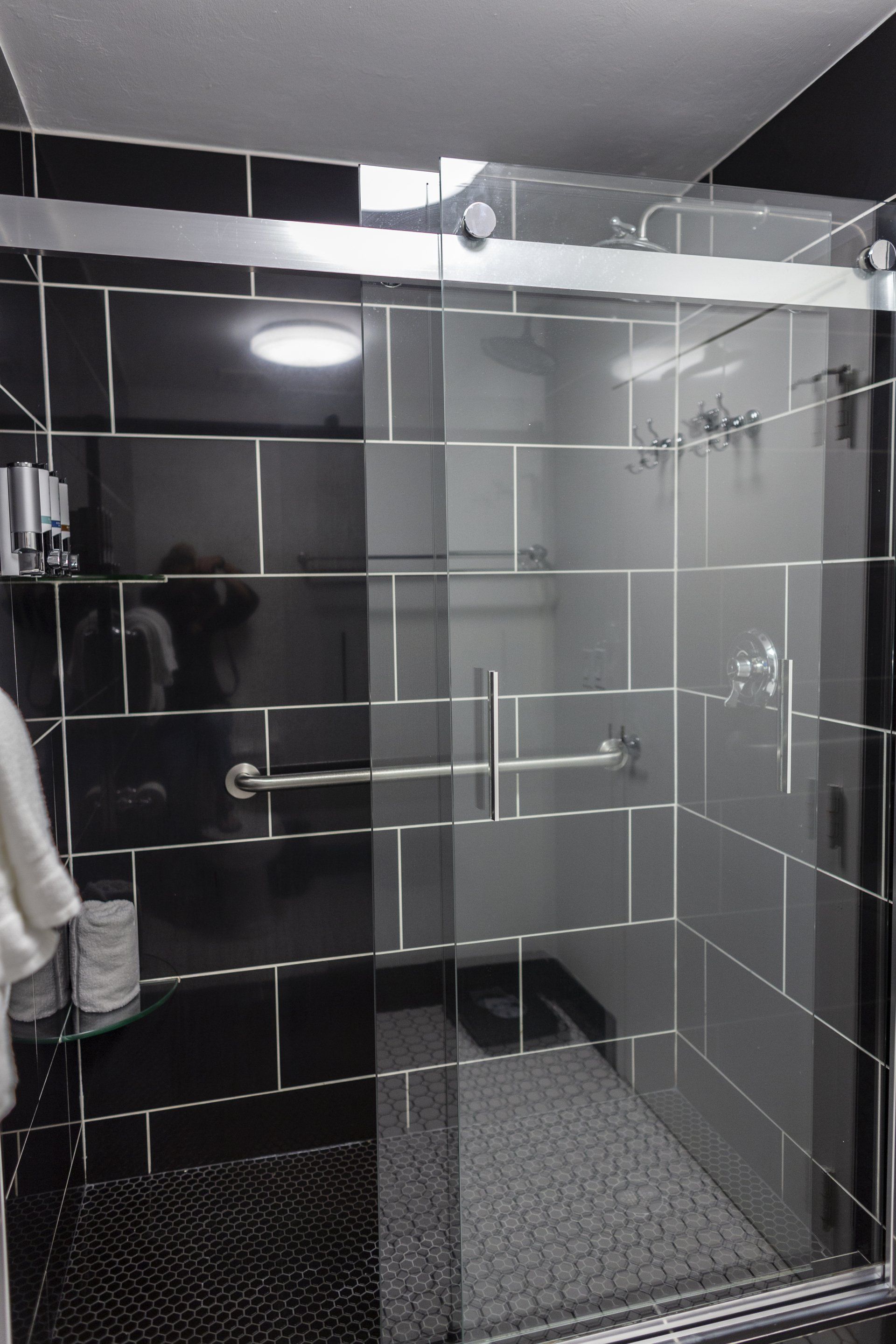A bathroom with black tiles and a sliding glass shower door