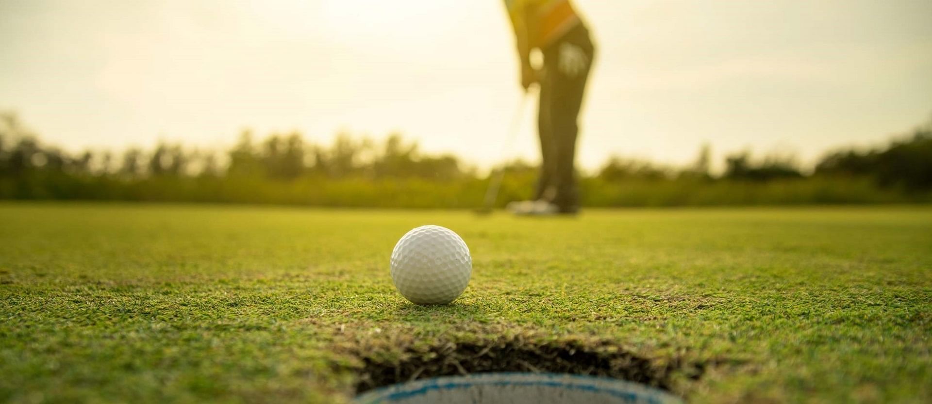 A golfer is putting a golf ball into a hole on a golf course.