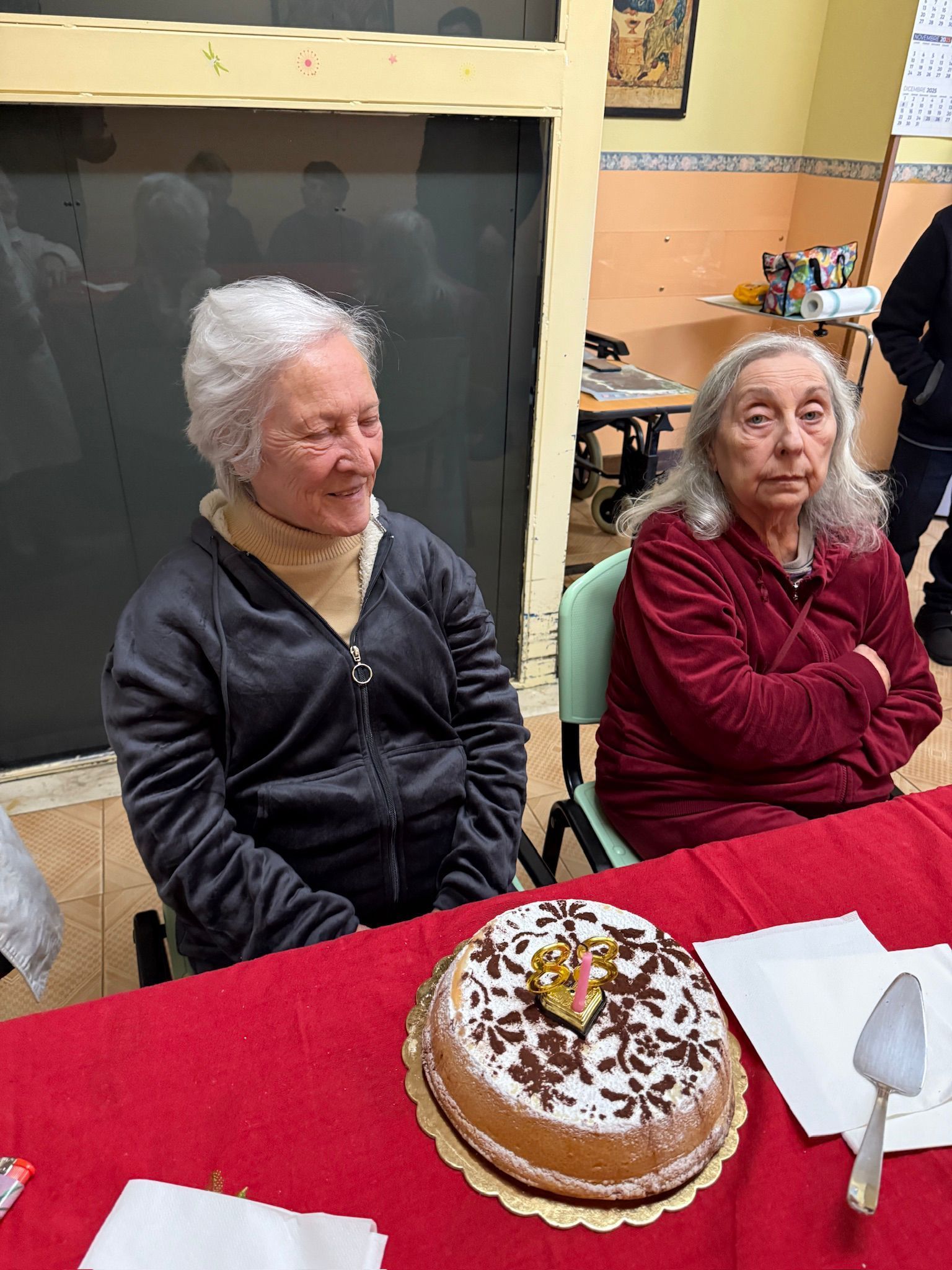 Due anziane signore sedute a un tavolo con una torta decorata davanti a loro.