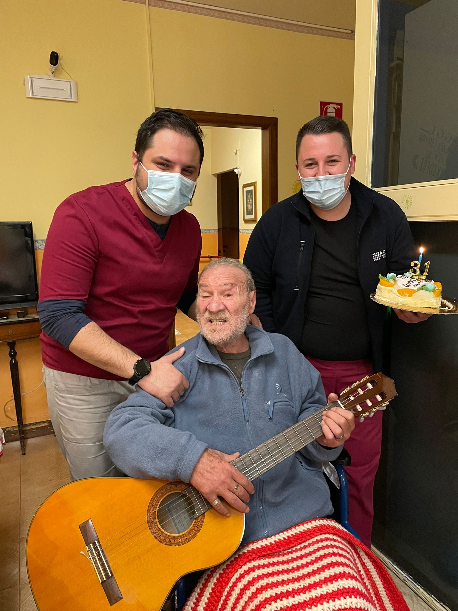anziano con la chitarra e assistenti con torta di compleanno