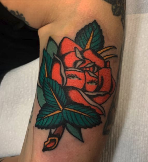 A tattoo of a red rose with green leaves on a person 's arm