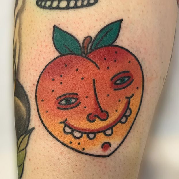 A person has a tattoo of an apple with a face on it.