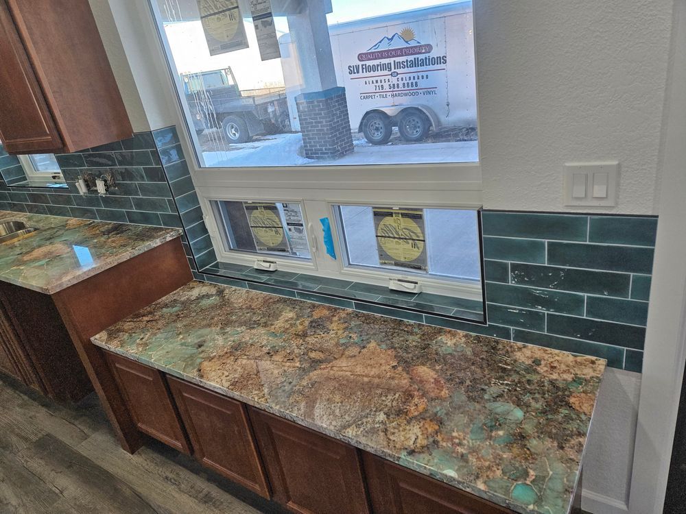 Kitchen with brown cabinets, green granite countertop, and teal subway tile backsplash near a window.